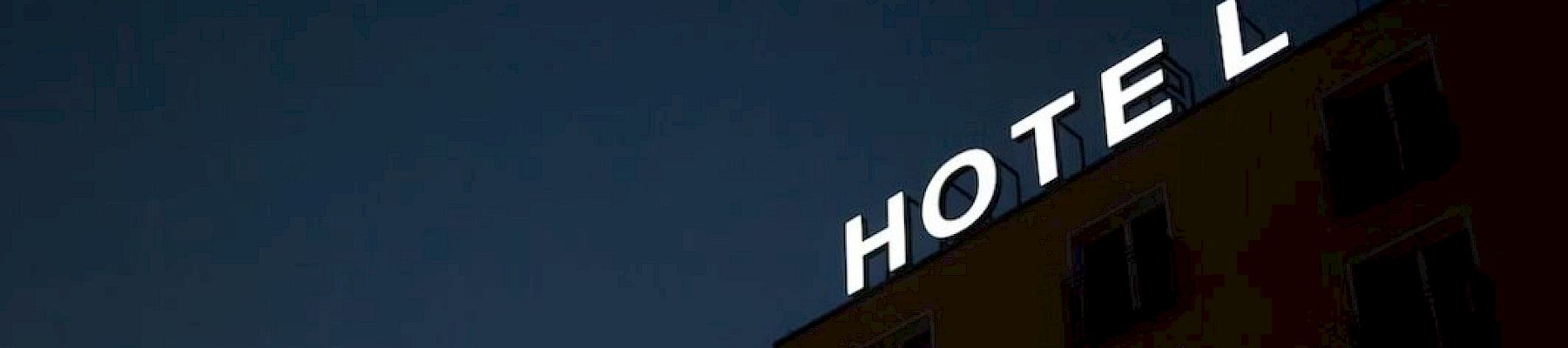 A nighttime hotel sign reading &ldquo;HOTEL&rdquo; on the side of a building against a dark blue sky.
