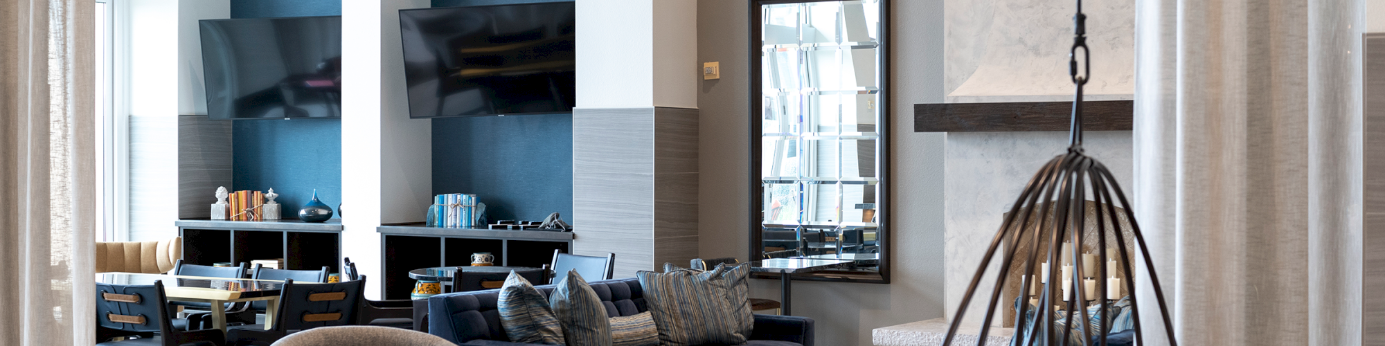 Modern living room with sofas, chairs, a gold chandelier, TV niches, dining area, and large windows behind curtains.