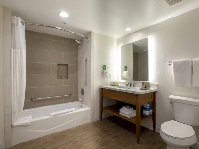 A modern bathroom with a bathtub/shower combo, a wooden vanity with a sink and mirror, towels on a rack, and a toilet.