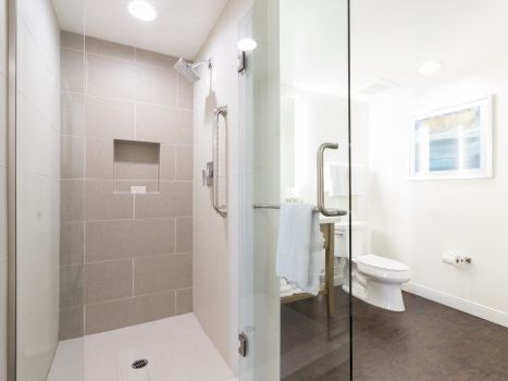 A modern bathroom with a glass-walled shower, beige tiles, a white toilet, and a towel hanging on a chrome rail, all in a bright, clean space.