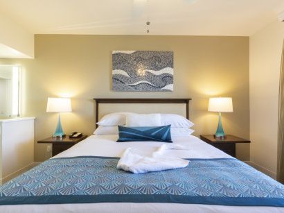 A neatly made hotel bed with two nightstands, lamps, a blue throw blanket, and wall art above the headboard, in a cozy room. Ends with a period.