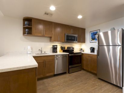 A modern L-shaped kitchen with wooden cabinets, stainless appliances, a beige countertop, and a stainless fridge, microwave, and range, all neatly arranged.