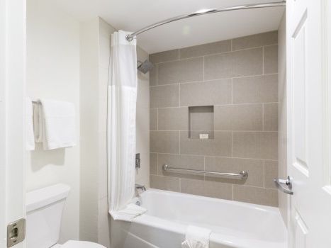 A compact bathroom with a white toilet, bathtub, gray tile wall, and a curved shower rod with a white curtain, neatly organized.