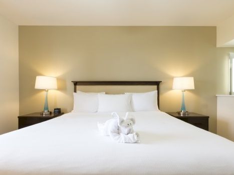 A clean hotel bedroom with a large bed, two nightstands and lamps, a folded towel sculpture in the center, and soft ambient lighting.