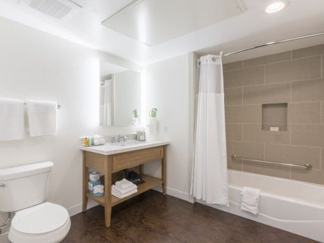 A clean bathroom with a toilet, wooden vanity, sink, towel rack, and a bathtub/shower combo with a built-in niche and white shower curtain.