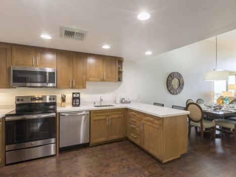 A modern kitchen with wooden cabinets, stainless steel appliances, white countertops, and an adjoining dining area with a round table and chairs.