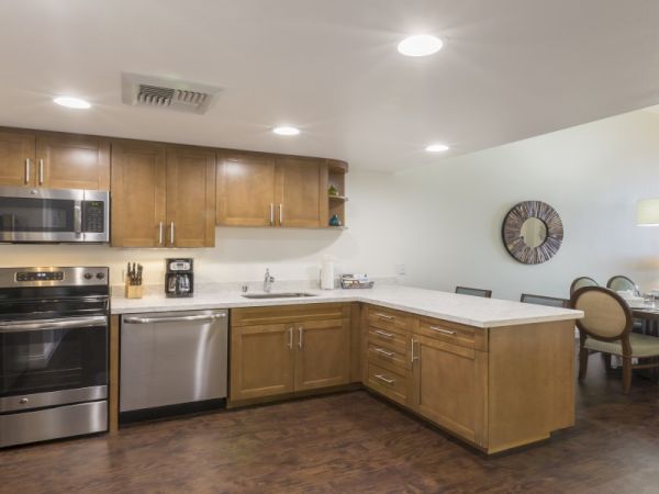 A modern L-shaped kitchen with wooden cabinets, stainless steel appliances, and a dining area visible in the background.