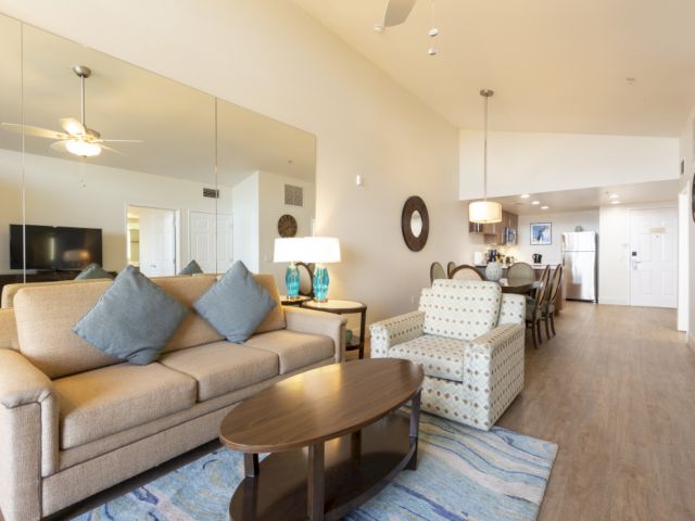 A bright modern living/dining room with a beige sofa, coffee table, TV, and dining chairs under pendant lights.