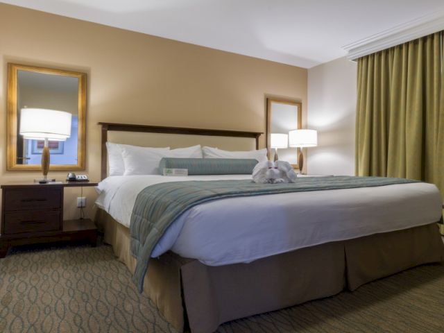 A cozy hotel room with a large bed, two nightstands, a desk, a chair, and warm lighting in a softly colored space.