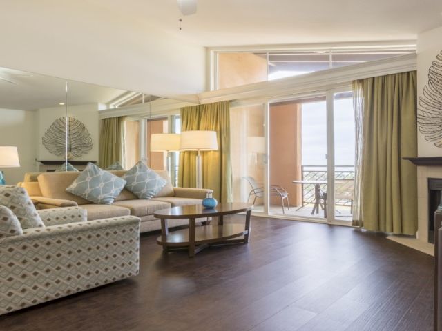A bright, open-plan living room with a cozy seating area, a glass coffee table, and modern decor in neutral tones.