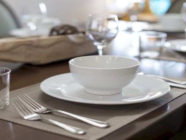 A neatly set dining table with white plates, silverware, and folded napkins, ready for a formal meal.