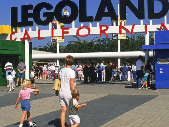 A busy LEGOLAND California entrance with the LEGO sign, colorful buildings, and children walking in the plaza.
