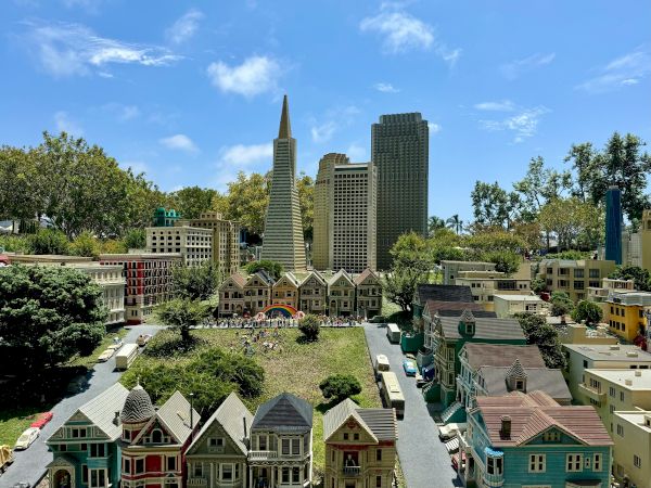 A vibrant cityscape of a miniature town with colorful houses in the foreground and tall modern skyscrapers in the background under a bright blue sky.