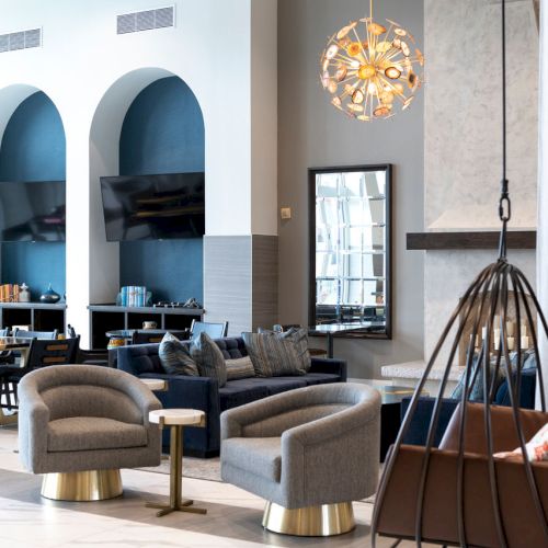 Modern living room with blue arches, sofa, coffee table, dining area, and a hanging chandelier.