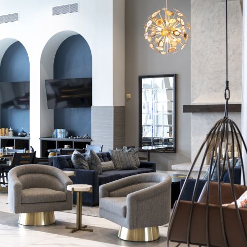 A stylish living room with a gray sectional, blue accent niches, a chandelier, dining chairs, and a hanging floor lamp.