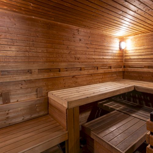A wooden sauna interior with built-in benches and a ceiling light glowing above the warm tiled floor.