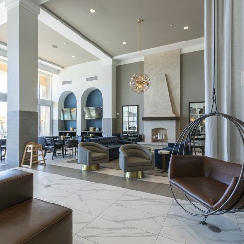 Modern hotel lobby interior with sofas, chairs, a fireplace, large windows, and a hanging chandelier.