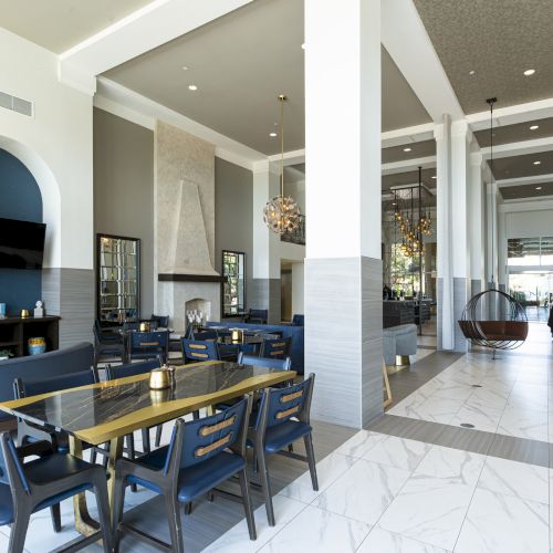 Bright hotel lounge with marble floors, blue chairs, chandeliers, and a reception area in the background.