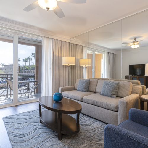 Bright modern living room with a sofa, coffee tables, TV, lamps, ceiling fans, and large sliding doors opening to a patio.
