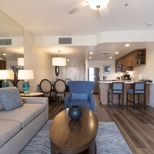 Bright modern living room with sofa, dining chairs, and a kitchen island with bar stools under ceiling lights.