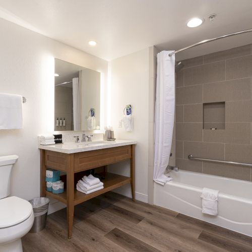 Modern bathroom with a toilet, vanity sink, folded towels, and a bathtub with shower curtain and safety grab bar.