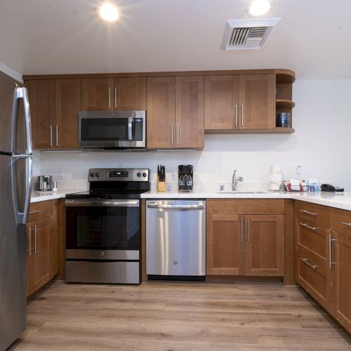 A modern kitchen with wood cabinets, stainless fridge, microwave, stove, dishwasher, and a countertop sink.