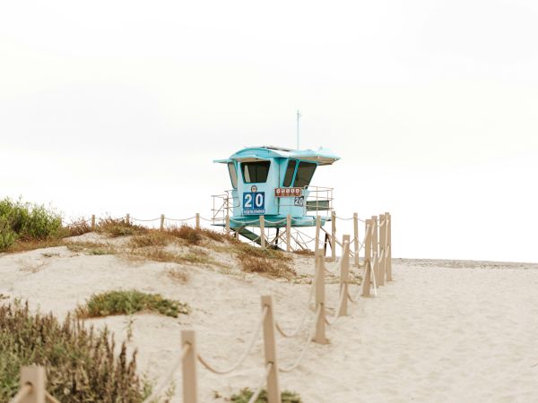 A teal lifeguard tower stands on a sandy dune near the beach, with the number 20 on the front and a lookout above.